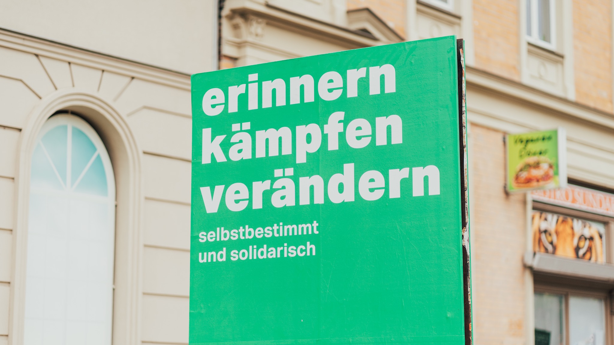 Straßenzug in Halle (Saale). Im Vordergrund ein aufgestelltes Banner: Vor grünen Hintergrund die weiße Aufschrift: "erinnern kämpfen verändern selbstbestimmt und solidarisch"