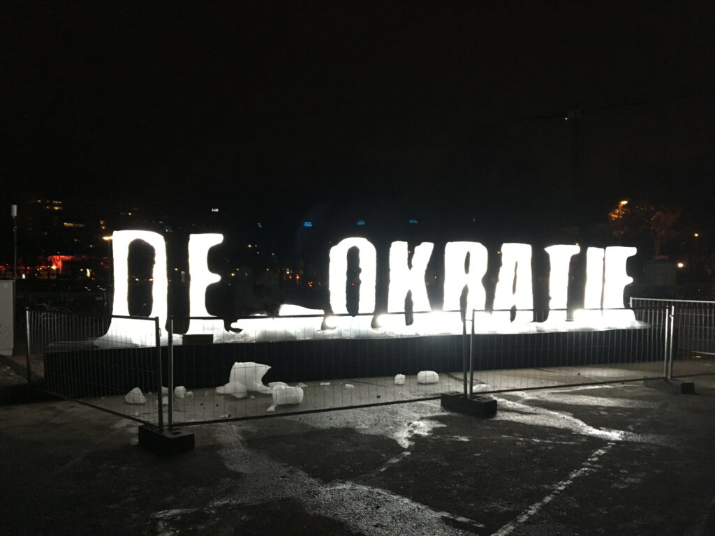 Photo of the lettering Democracy: The letters formed from ice, the M loves broken next to it, so that you can read: "DE OKRATIE"